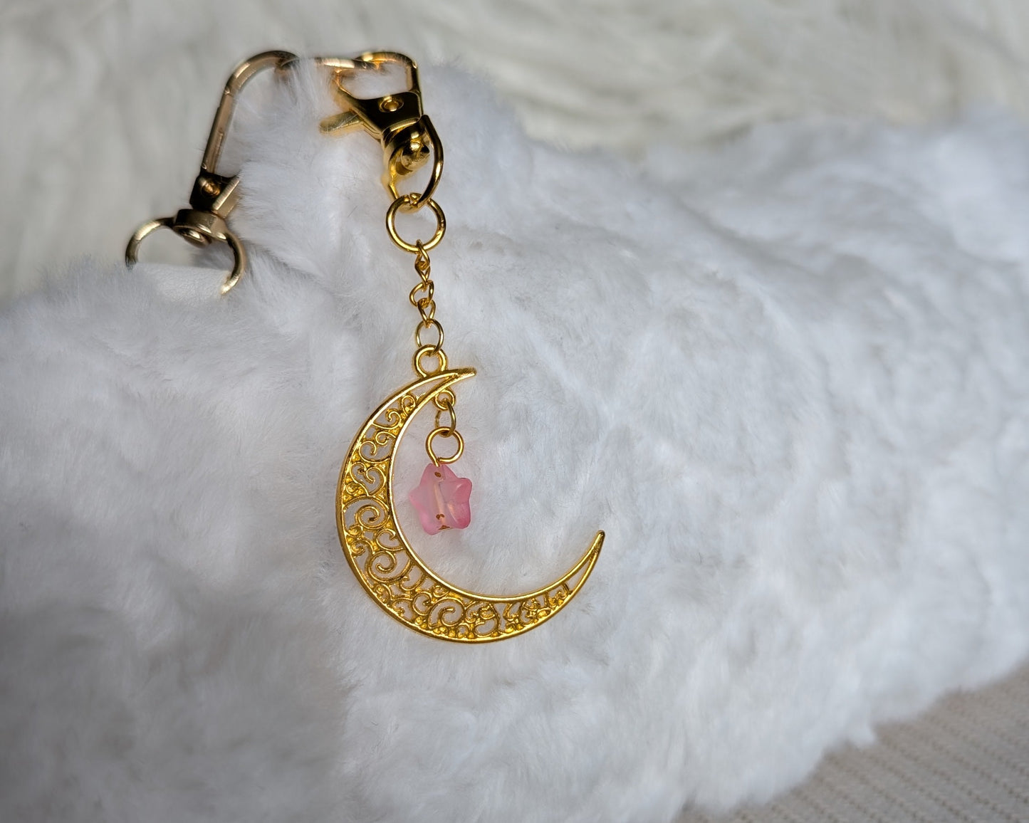 Gold crescent moon earring with pink gemstone on a white fabric background