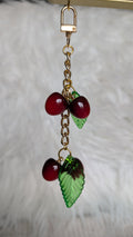 Cherry and leaf charm on a gold chain against a neutral background