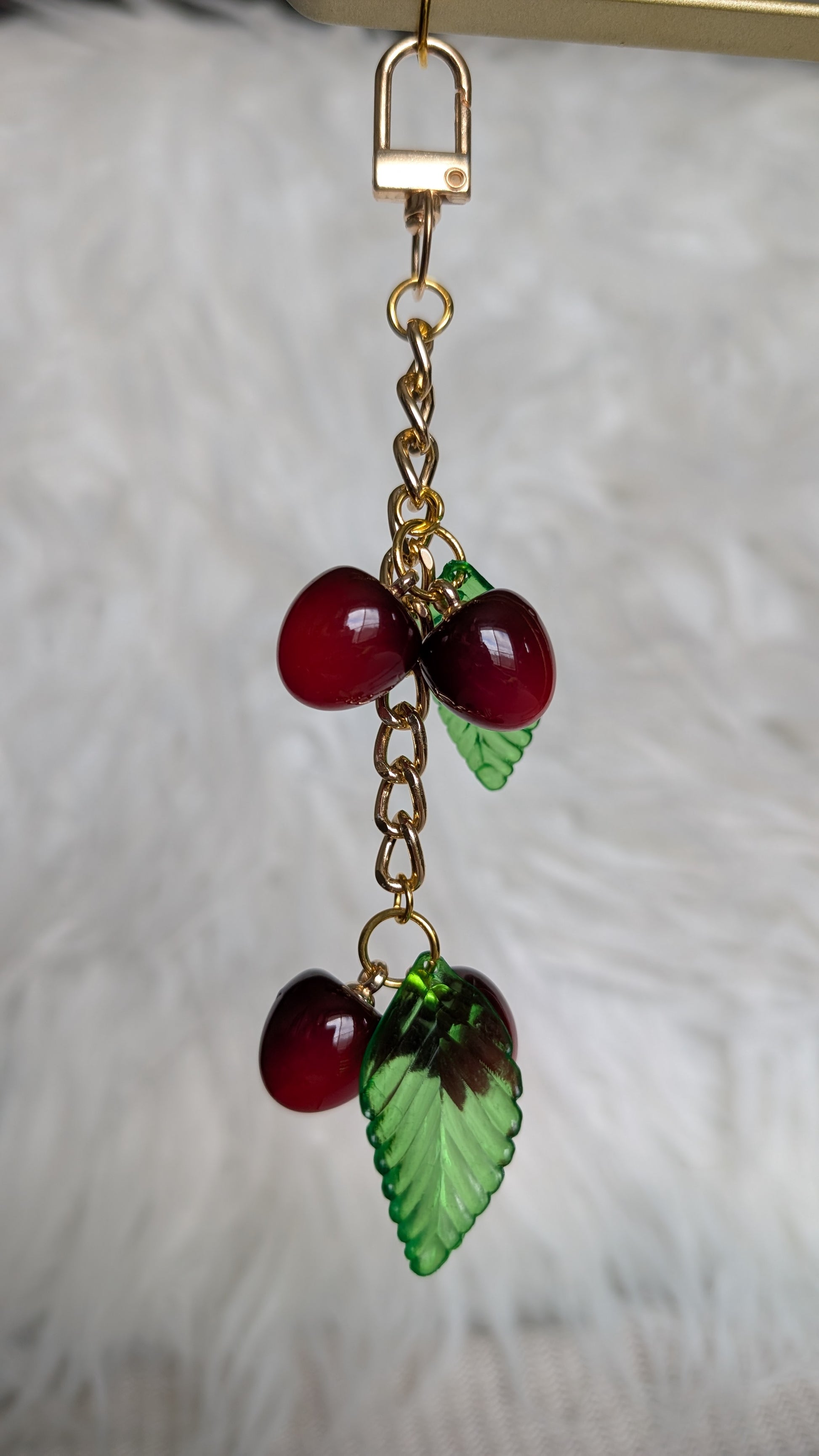 Cherry and leaf charm on a gold chain against a neutral background
