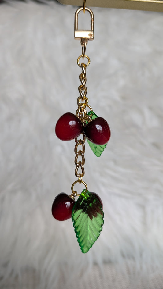Cherry and leaf charm on a gold chain against a neutral background