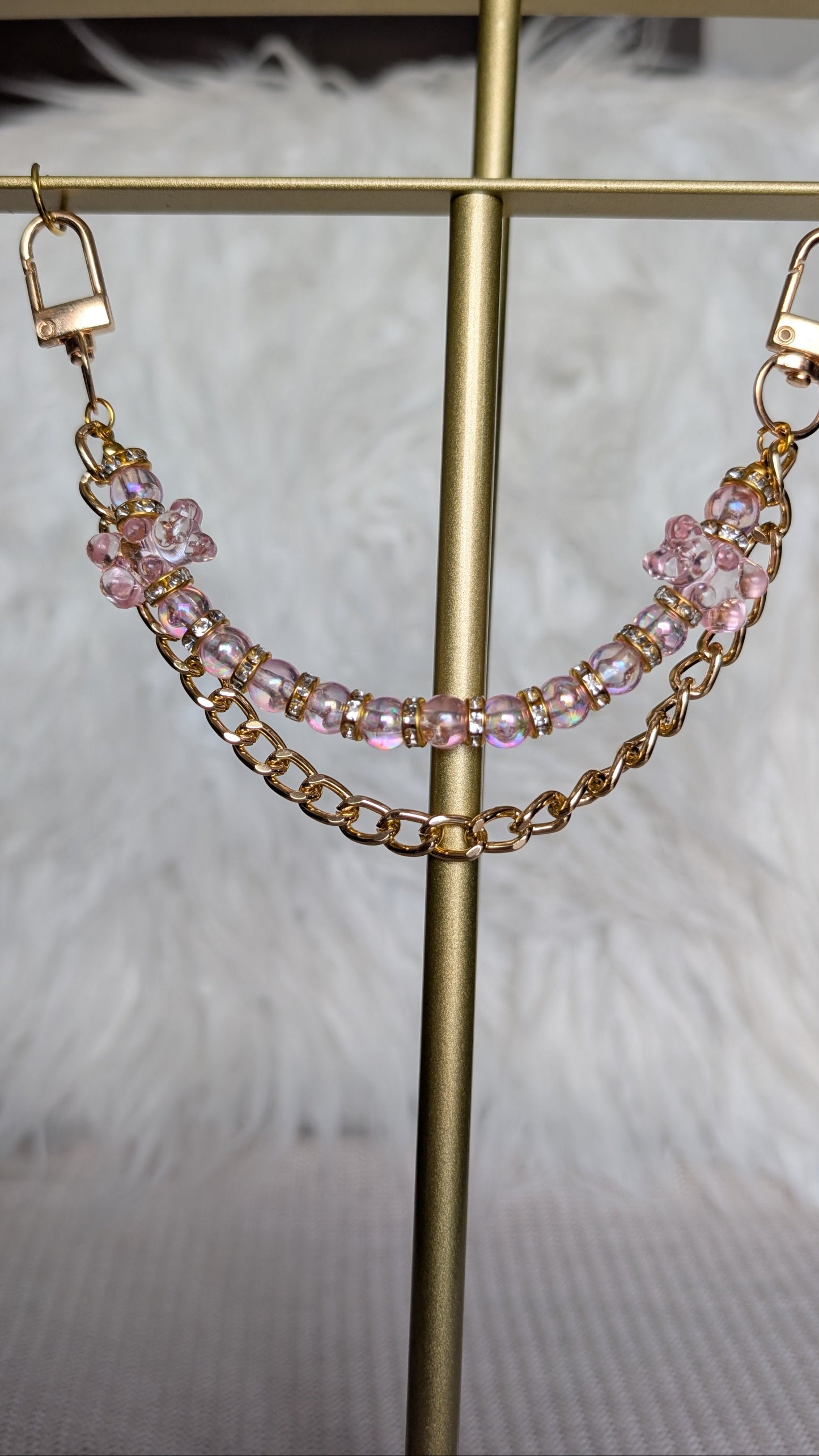 Gold chain and pink beaded earrings on a gold stand with a soft white background