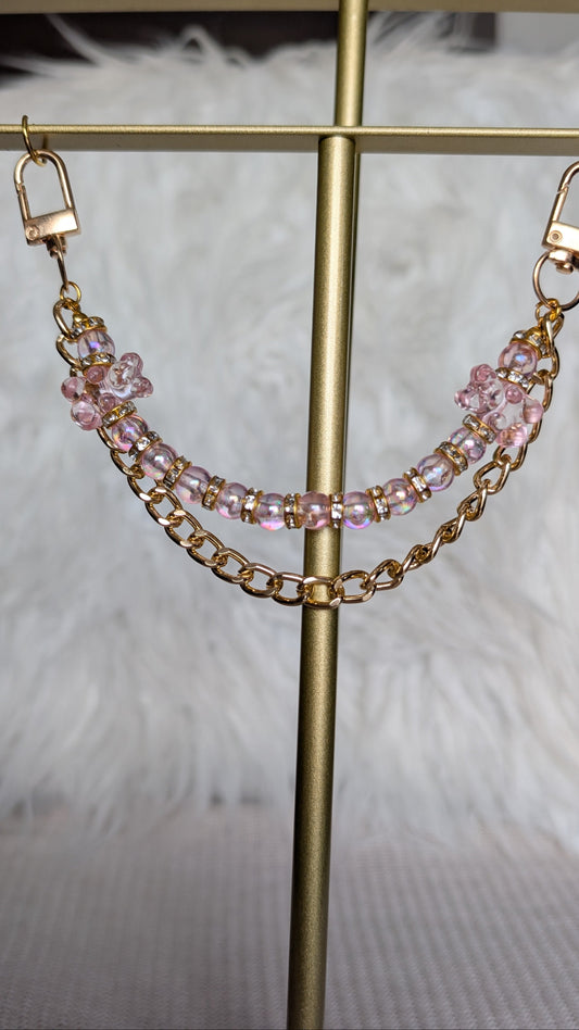 Gold chain and pink beaded earrings on a gold stand with a soft white background