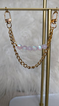 Gold chain and pink beaded earring on a gold stand with a white feather background