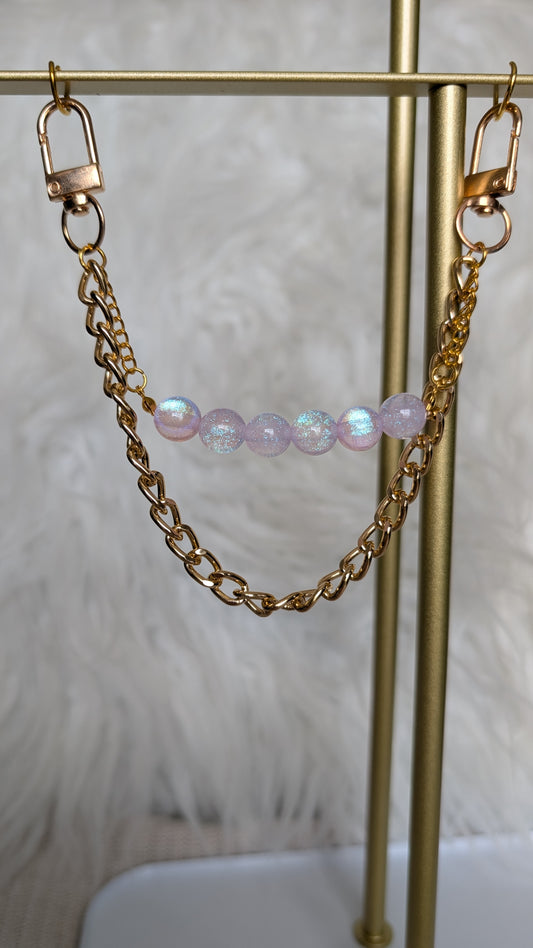 Gold chain and pink beaded earring on a gold stand with a white feather background
