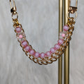 Gold chain bracelet with pink beads on a stand against a neutral background
