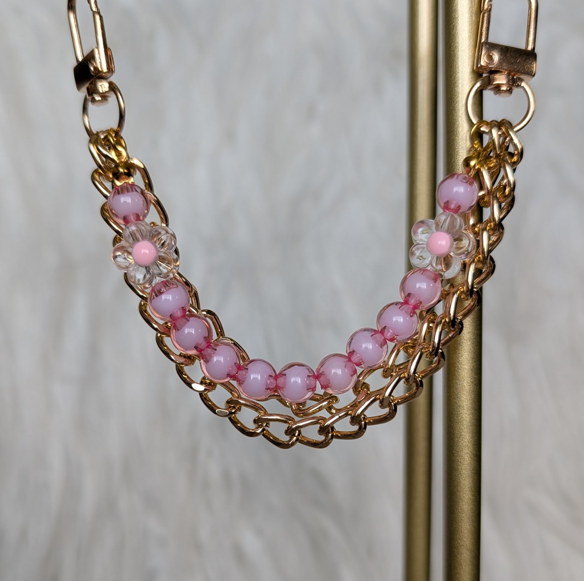 Gold chain bracelet with pink beads on a stand against a neutral background