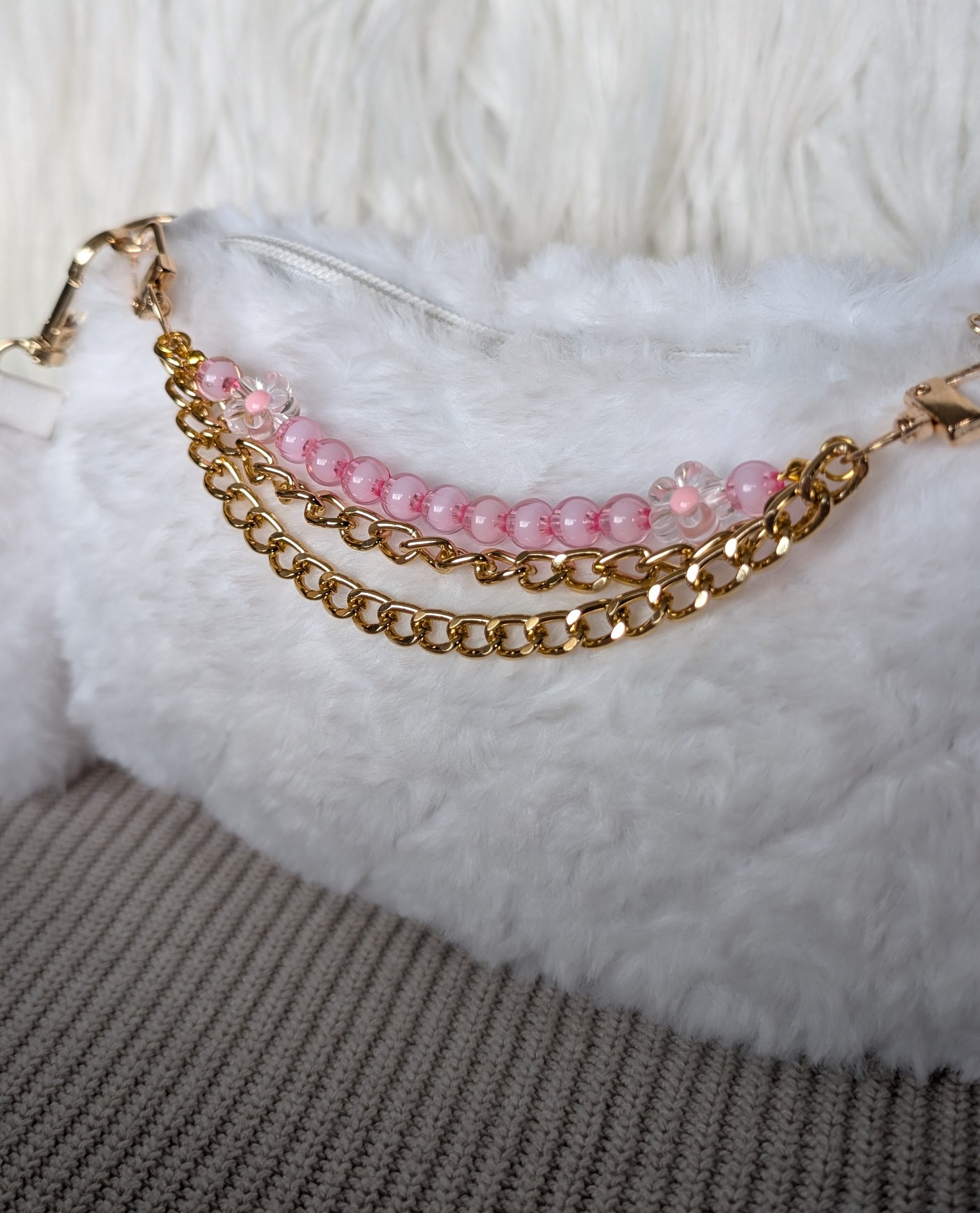 Gold chain and pink beaded bracelet on a white fur surface