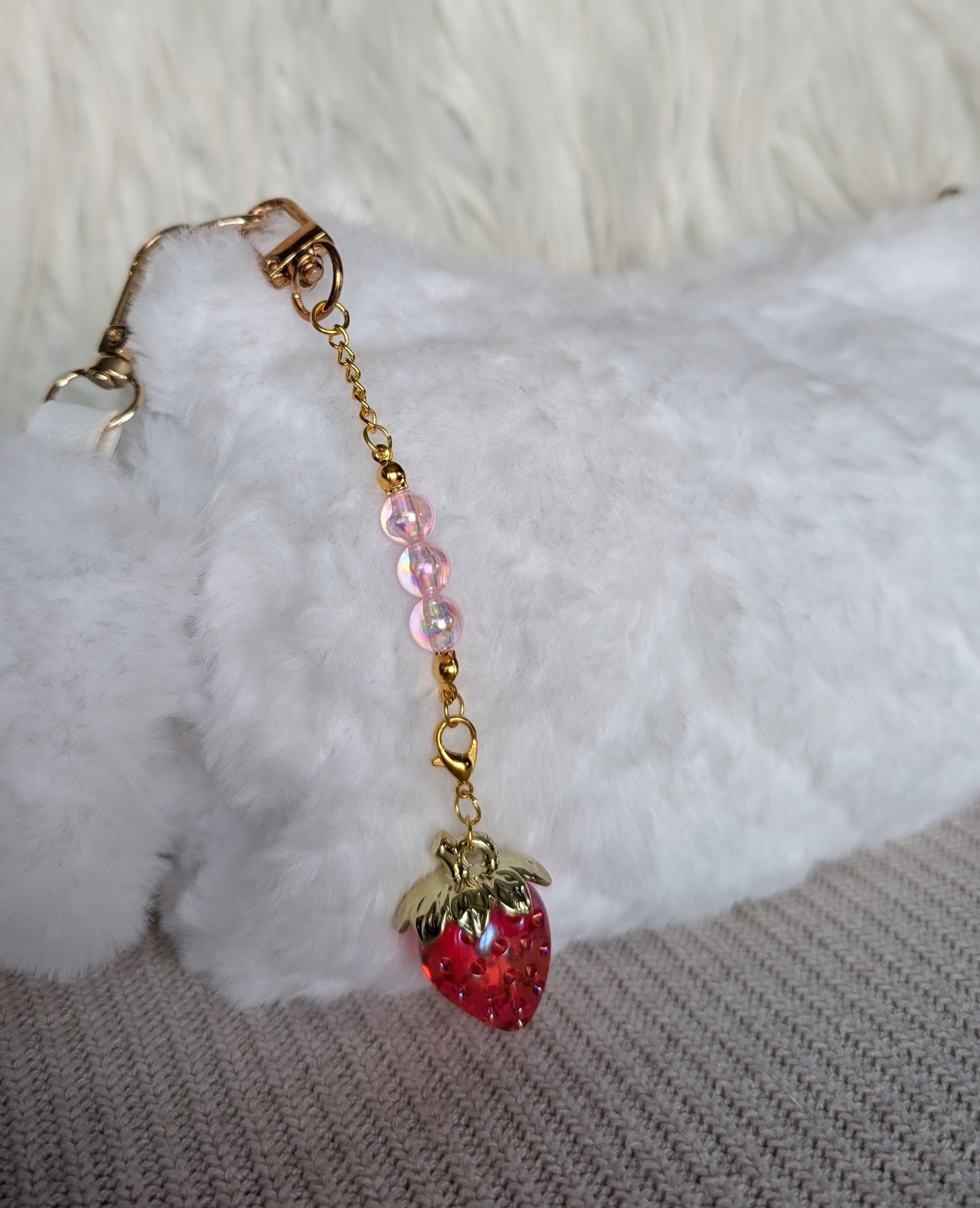 Strawberry-shaped charm with pink beads on a gold chain against a white fur background