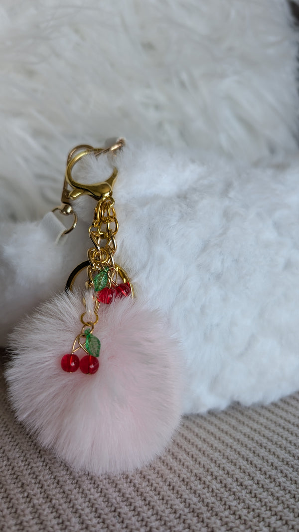 Pink fluffy keychain with gold chain and red beads on a white fur background