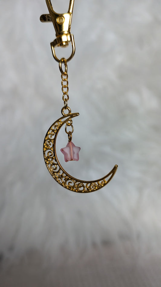 Gold crescent moon keychain with pink star charm on a soft gray background