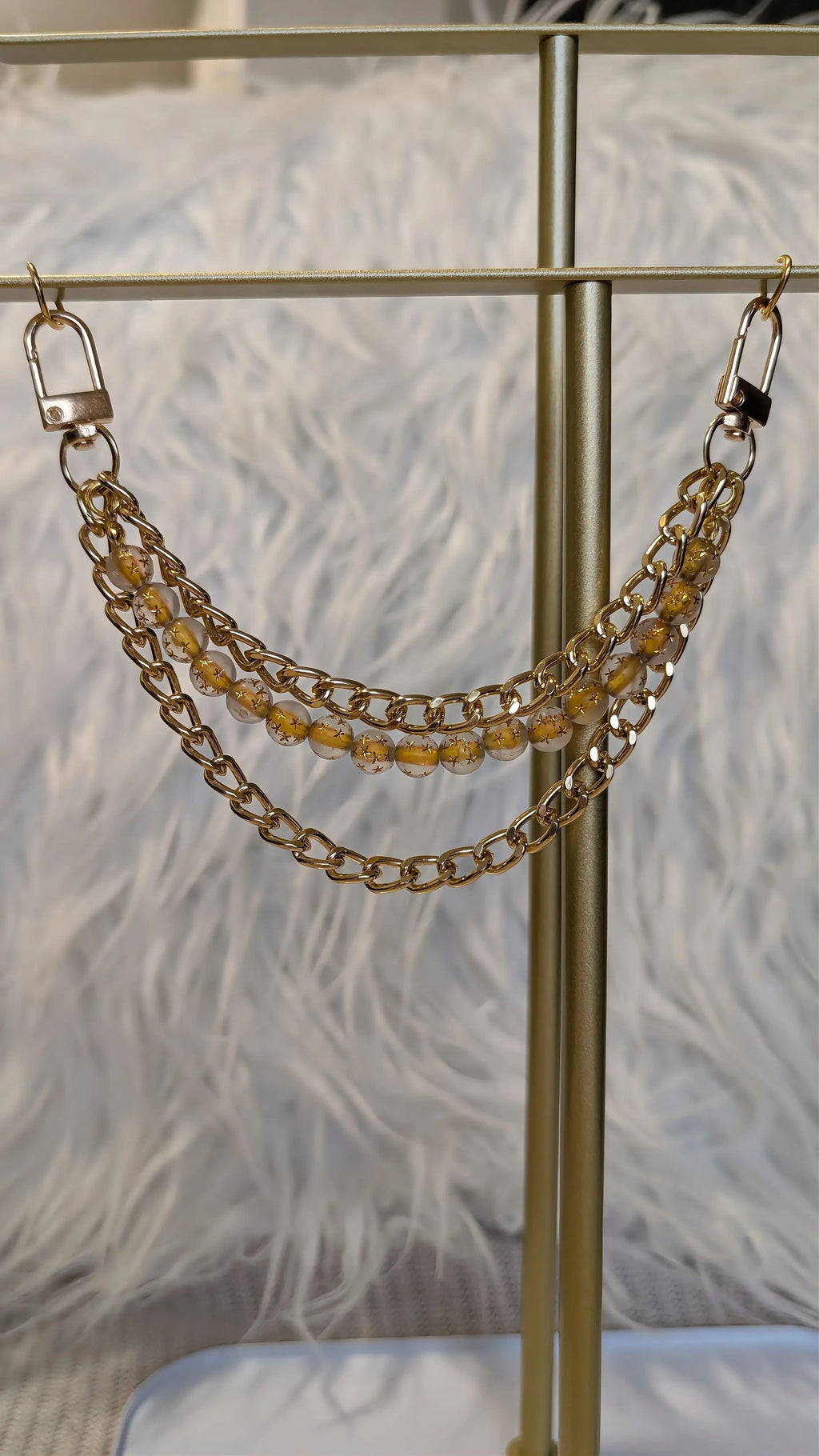 Gold chain accessory on a stand with a feathered background