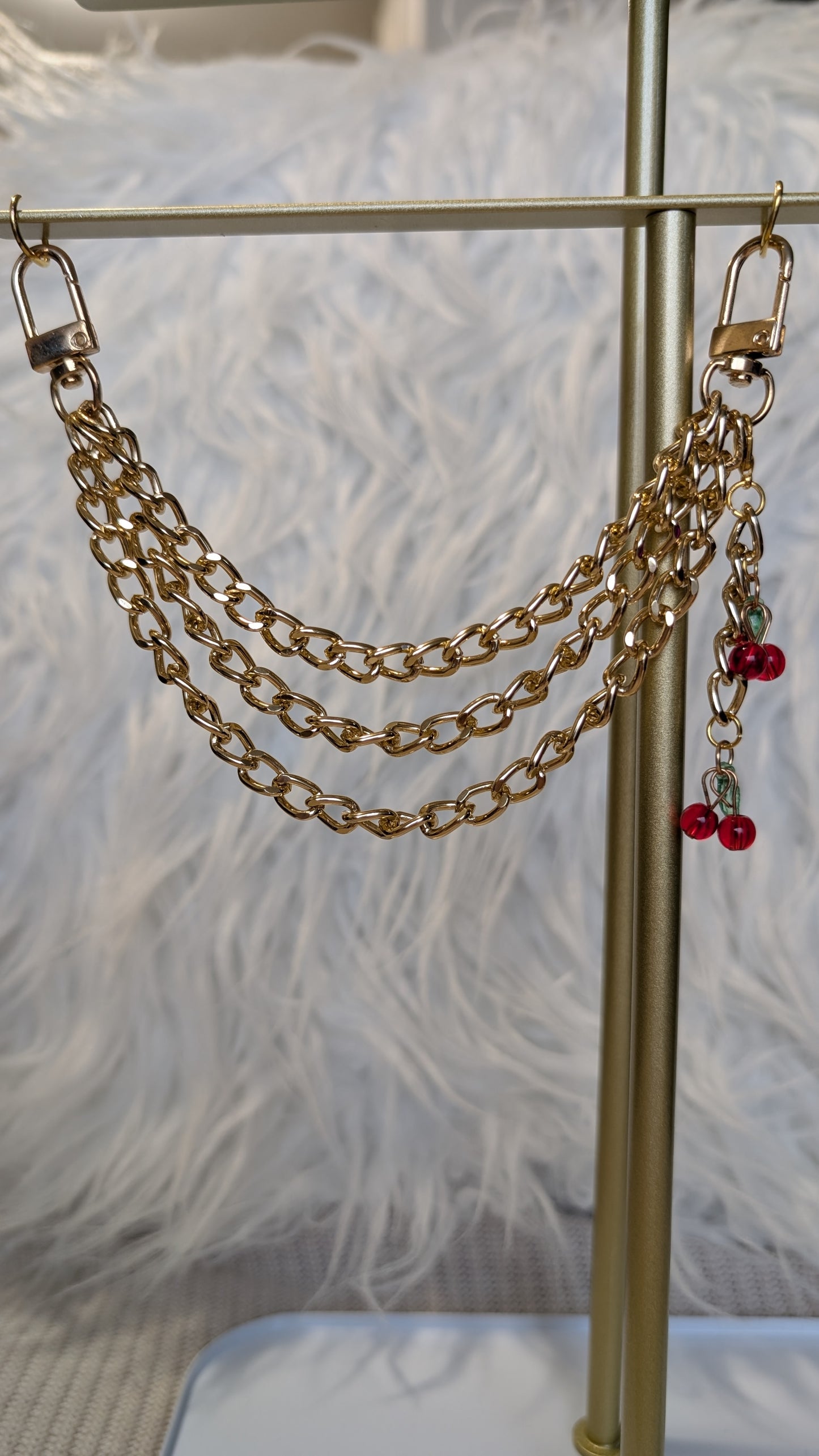 Gold chain accessory with red charms on a stand against a textured white background