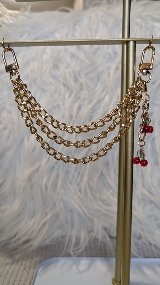 Gold chain accessory with red charms on a stand against a textured white background